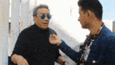 a man wearing sunglasses is being interviewed by a man in a denim jacket