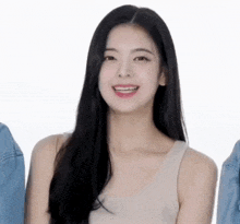 a woman with long black hair is smiling for the camera while wearing a white tank top .