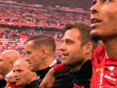 a group of men are watching a soccer game and one of them is wearing a red shirt that says league