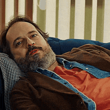 a man with a beard is laying on a couch and looking at the camera
