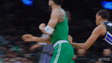 a basketball player in a green jersey is dribbling the ball while another player tries to stop him .