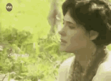 a woman in a white dress is sitting in the grass looking at something .
