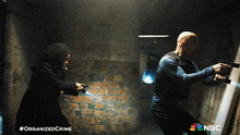 a man and a woman holding guns in a dark room with the nbc logo visible