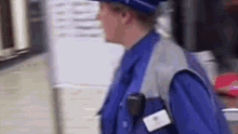 a man wearing a blue vest and a blue hat is standing in a store .