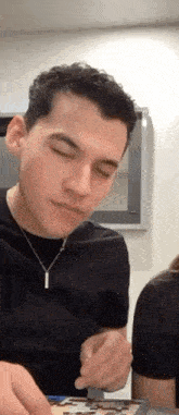 a man in a black shirt is sitting at a table with his eyes closed and eating a piece of cake .