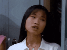 a woman in a white shirt and necklace is standing in front of a locker