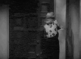 a woman in a floral shirt is standing in front of a door in a black and white photo .