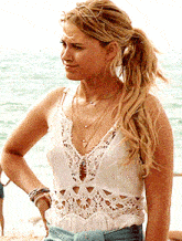 a woman wearing a white lace top and denim shorts stands on a beach