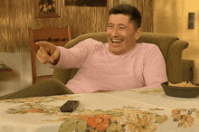 a man in a pink shirt is sitting in a chair pointing at the camera