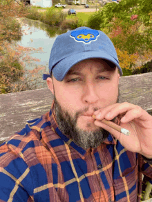 a man smoking a cigar wearing a blue hat with a bear on it