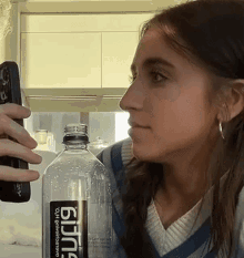 a woman holding a remote control next to a bottle of bjing