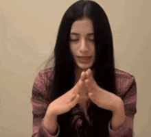 a woman with long black hair is praying with her hands folded in front of her face .