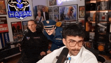 a man in a police uniform talks into a microphone in front of a hasan sign