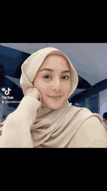 a woman wearing a hijab and a white sweater has tiktok written on the bottom right corner