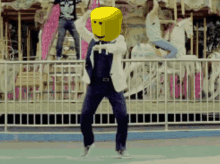 a man with a yellow face on his head dancing in front of a merry go round
