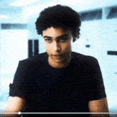 a young man with curly hair wearing a black t-shirt is looking at the camera .