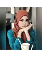a woman wearing a hijab sits at a table with a mcdonald 's cup in front of her