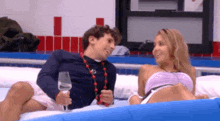 a man and a woman are sitting on a bed holding wine glasses .