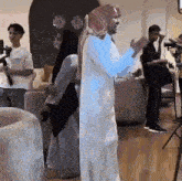 a man in a white robe is standing in a living room with a woman in a hijab .