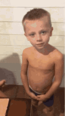a shirtless young boy is standing in front of a cake on a table .