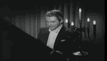 a man in a tuxedo and bow tie is playing a piano in front of a chandelier .