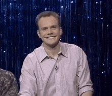a man in a pink shirt is smiling in front of a blue curtain with stars .