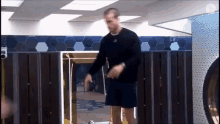 a man in a black sweater and shorts is standing in a locker room .