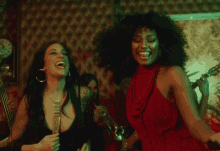 a woman in a red dress laughs while another woman plays a guitar