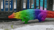 a rainbow colored crocodile is in a cage with a blue fence in the background