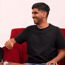 a man in a black t-shirt is sitting on a red couch
