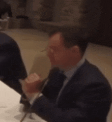 a man in a suit and tie is sitting at a table with a microphone .