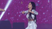a woman in a crop top and skirt is dancing on a stage with her arms in the air .