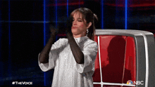 a woman wearing a white dress and black gloves is applauding while sitting in a chair .