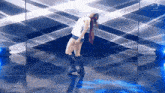 a woman in a white tank top and shorts is dancing on a stage in front of a mirror .