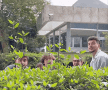 a group of people are standing in front of a building behind a bush