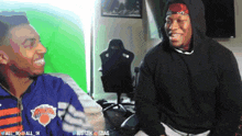 a man wearing a knicks jacket is laughing with another man
