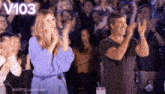 a man and a woman are applauding in front of a crowd of people .