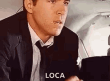 a man in a suit and tie is sitting in the back seat of an airplane talking to someone .