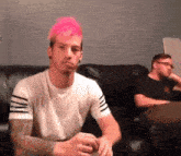 a man with pink hair is sitting on a black couch