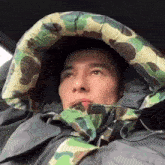 a man is wearing a camouflage jacket with a hood and sleeping bag .