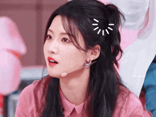 a girl wearing a pink shirt and a microphone has a drawing of a sun on her head
