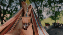 a person sitting in a hammock holding a cup of coffee that says trump