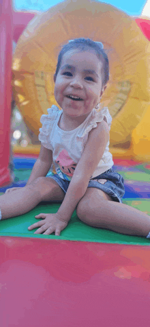 a little girl is sitting on a colorful mat in front of an inflatable slide .