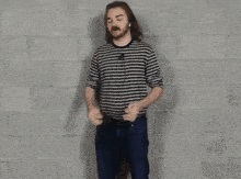 a man with long hair and a beard is wearing a striped shirt and jeans