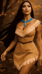 a woman in a native american dress and necklace is walking through the woods .