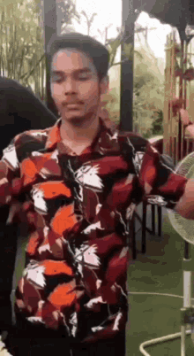 a young man in a floral shirt is standing in front of a fan .