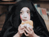 a woman wearing a black veil is eating a hamburger with the watermark meijurugui