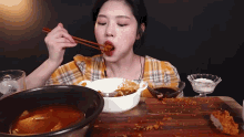 a woman is eating food with chopsticks and a bowl of food on a table .