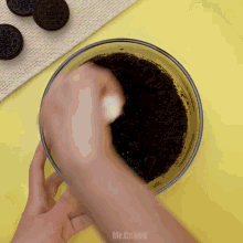 a person is mixing oreos in a bowl with a yellow background