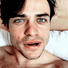 a shirtless man with blue eyes is laying in bed